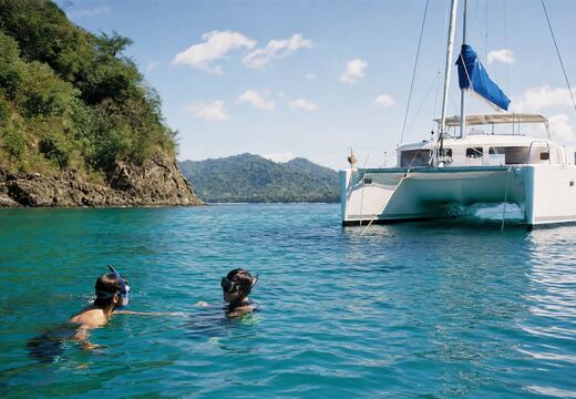 Snorkelers in clear water beside a moored catamaran.